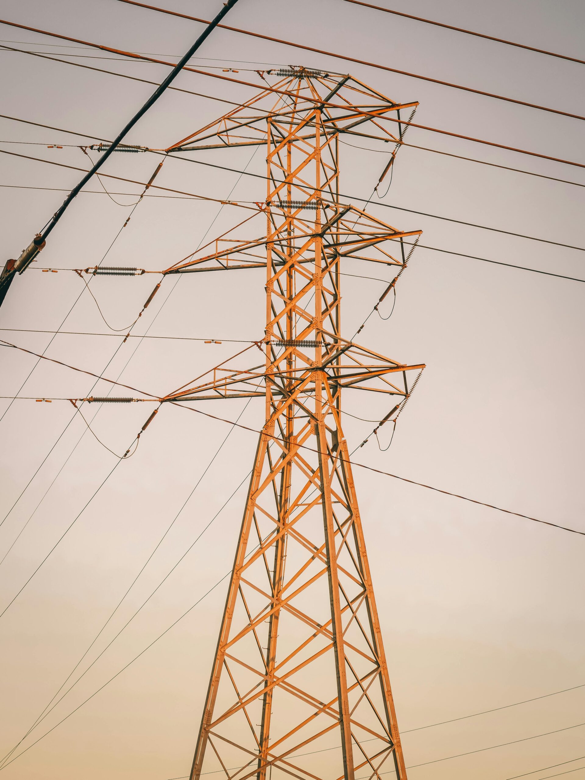 A tall steel transmission tower under soft sunset light casting shadows.